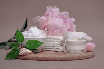 on a wooden stand white skin care cream, white clean towels, pink peony, white jar and sponge, skin and body care, spa set