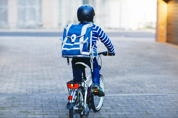 Schoolkid boy in safety helmet riding with bike in the city with backpack. Happy child in colorful clothes biking on bicycle on way to school. Safe way for kids outdoors to school