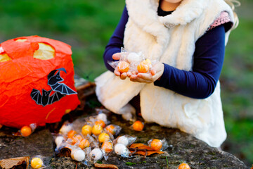 Closeup of toddler girl trick or treating on Halloween. Happy child outdoors counting sweets from...