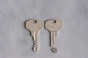 Two broken and whole keys on a gray textured background. Conceptual symbolic image