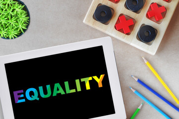 Equality word on digital computer tablet with colored pencils and tic tac toe game on workspace...
