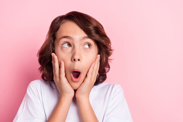 Photo of shocked amazed young small boy hold hands cheeks look empty space isolated on pink color background