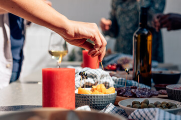 female hand holding toothpick piercing a piece of melon on party table with aperitif snacks. Incidental people in the foreground. - obrazy, fototapety, plakaty