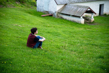 Naklejka na ściany i meble Young person sits alone in a grassy field looking into the distance