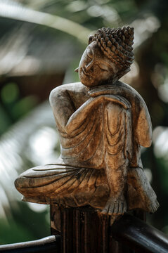 Statuette of Buddha on a background of green leaves close up.