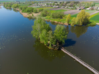 Obraz premium Island on pond with footbridge, hut and trees, aerial view