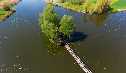 Island on pond with footbridge, hut and trees, aerial view