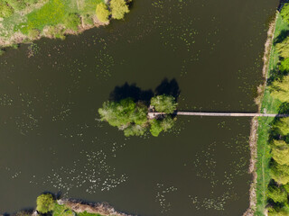 Island on pond with footbridge, hut, trees, vertical aerial view