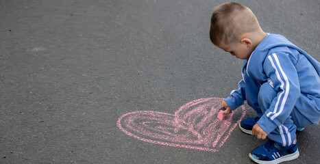 Fototapeta premium Cute little child draws with chalk outdoors, summer time, chalk. Selective focus.