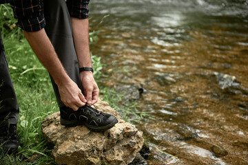Tourist tying shoelaces placing his foot on a large stone by the stream