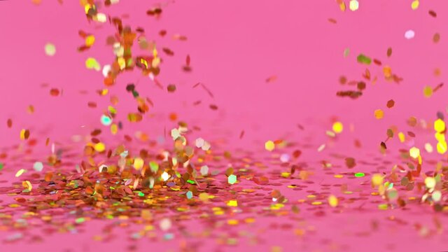 Super Slow Motion of gold confetti falling on a pink background. Filmed on high speed cinematic camera at 1000 frames per second.