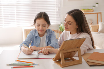 Mother helping her daughter with homework using tablet at home