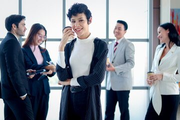 Smart and elegant smiling business woman lady boss with black short hair confidential standing and holding coffee paper cup at the window office workplace , four business people as blurred background.