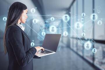 Pretty caucasian female using laptop with abstract glowing social networking concept hologram on blurry office interior background. Double exposure.
