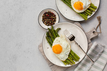 Asparagus with fried egg on white plate, top view, light grey background. Copy space.