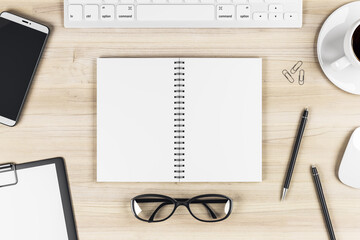 Stylish work table with blank notebook pages, keyboard, glasses, smartphone and coffee mug on wooden surface. Mock up