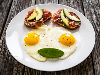 Continental breakfast - sunny side up eggs and crudo sandwiches with avocado on wooden table