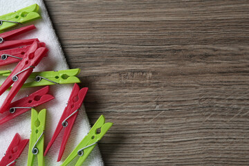 Colorful plastic clothespins and towel on wooden background, top view Space for text