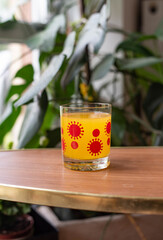 Mid-century modern glass with orange juice - with corona virus pattern - on a wooden table with plants in the background