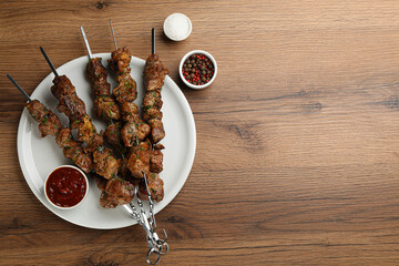 Metal skewers with delicious meat, ketchup and spices served on wooden table, flat lay. Space for text