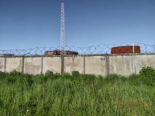 Industrial area outside the city. Oil storage tanks. Big tower. Fenced territory of the industrial zone with a fence with barbed wire.