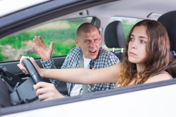 Confused young woman driving car against background of angry screaming man sitting in passenger seat - obrazy, fototapety, plakaty