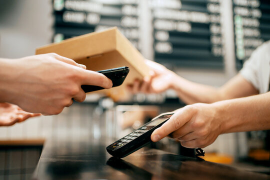 NFC payment phone gadget. The waiter is an employee of the bistro cafe working. Sells pizza in a paper-wrapped takeaway box.