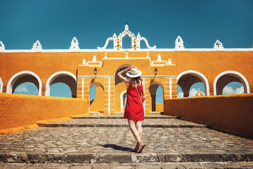 A young woman in a red dress and hat travels through the yellow city of Izamal, Mexico. Lifestyle. Travel to Mexico. Beautiful multicolored cities in Mexico