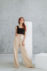 an attractive young red-haired woman in a black tank top and wide white stylish trousers. slim...
