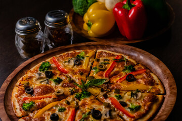Close up shot of tasty pizza with blurry colorful vegetables and sprinkler in the background.