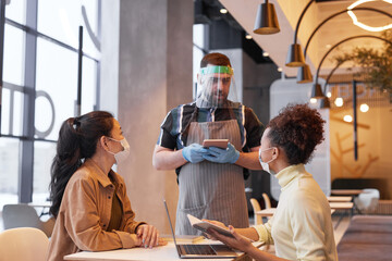 Waist up portrait of waiter wearing face shield while taking order in cafe with covid safety measures, copy space