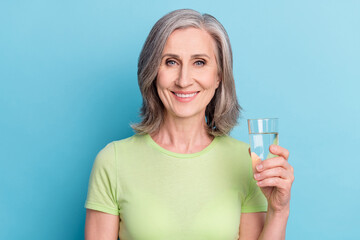 Photo of charming cheerful happy old woman hold hand glass of water hydrated isolated on blue color background
