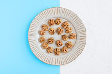 Walnuts in a plate on sky blue and white background, flat lay.