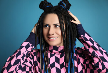 Beautiful young woman with nose piercing and dreadlocks on light blue background