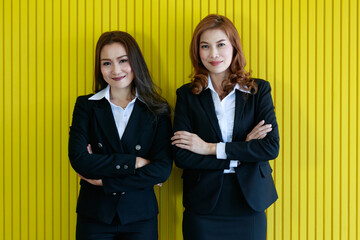 Positive Asian managers leaning on yellow wall