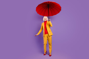 Full size photo of cheerful short hairdo aged lady hold umbrella wear yellow costume isolated on purple background © deagreez
