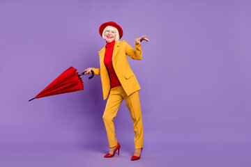 Full body profile photo of funny short hairdo elder lady wear yellow suit cap umbrella isolated on purple background