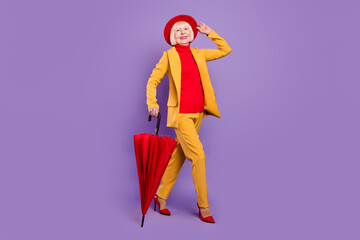 Full body profile photo of cheerful short hairdo aged lady go wear yellow suit cap umbrella isolated on purple background