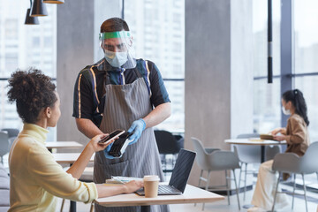 Waist up portrait of waiter wearing face shield and gloves while taking payment in cafe with covid safety measures, copy space