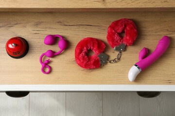 Different modern sex toys in open wooden drawer, top view