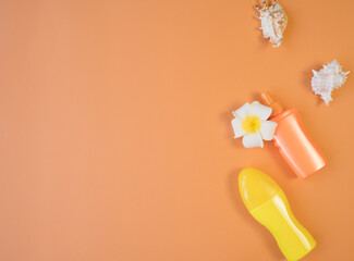 Two tubes of orange and yellow tanning cream, seashells, plumeria flower top view on an orange background. Template for the text on the left. Travel concept.