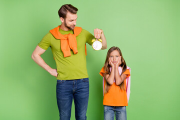 Obraz premium Portrait of nice upset people dad holding clock girl waking up early morning punctuality isolated over green color background