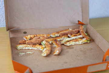 Leftover pizza in a cardboard box on a home table. Unhealthy high-calorie food