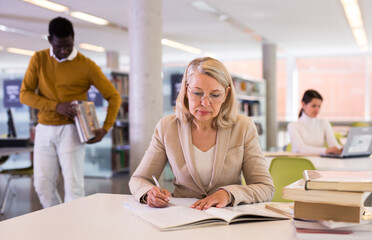 Fototapeta premium Woman with books sits at table in the library. High quality photo