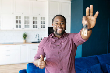 Own property. Positive overjoyed African-American guy shows keys from new house and thumb, bought...