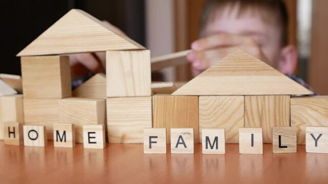 Home and family are real values. Active preschooler caucasian boy builds a house from wooden cubes. The inscription family and home on wooden details. The child plays at home. selective focus