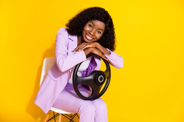 Fototapeta premium Photo of young happy beautiful cheerful positive afro woman sit chair hold steering wheel isolated on yellow color background