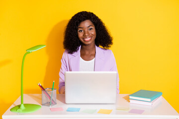 Photo of young happy positive smiling afro businesswoman sit table work in computer isolated on yellow color background