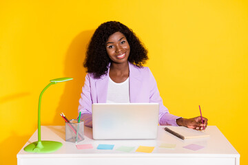 Photo of young happy positive smiling afro woman working in laptop writing in organizer isolated on yellow color background