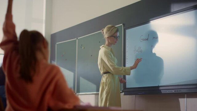 Teacher writing on interactive digital whiteboard. Students raising hands